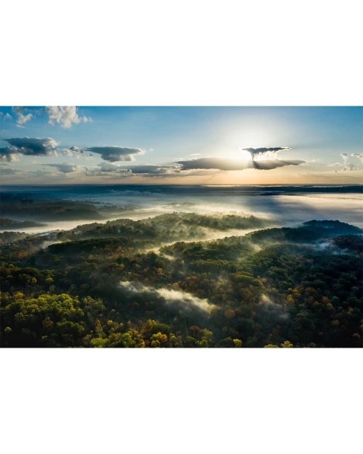 Aerial view of a misty forest landscape with morning sunlight filtering through the clouds, creating a tranquil and ethereal atmosphere.