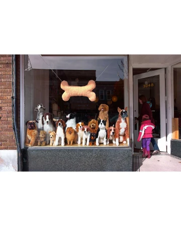 A storefront window displays a large collection of dog breeds as plush toys and a dog-bone decoration. A girl and woman enter the shop.
