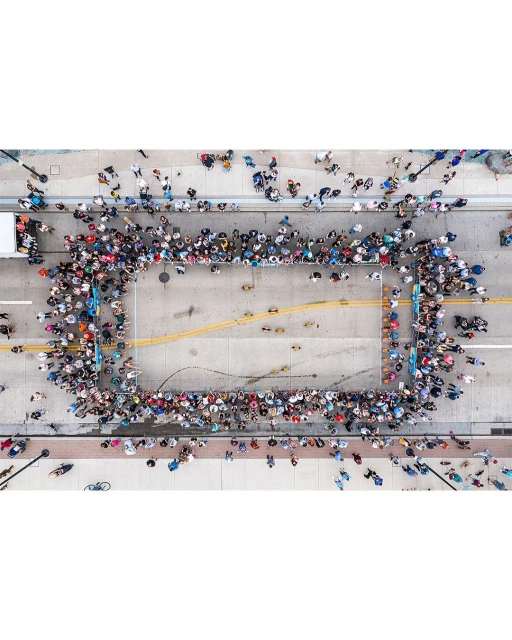 Aerial view of a large group of people gathered in an open street, forming a rectangular shape, captured with a high-angle perspective.