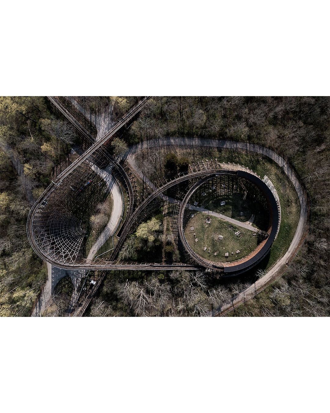 Aerial view of a wooden roller coaster winding through a densely wooded area, showcasing its curving tracks and structural design.