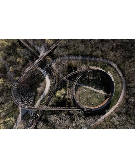 Aerial view of a wooden roller coaster winding through a densely wooded area, showcasing its curving tracks and structural design.