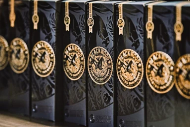 Close-up of several dark packaging boxes for Blackwood Toasted Bourbon with gold circular seals.