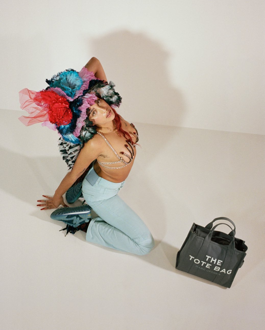 Woman with colorful headdress and light blue jeans kneeling in studio with gray Marc Jacobs tote bag and matching shoes, fashion shot.