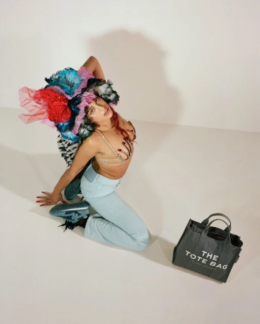 Woman with colorful headdress and light blue jeans kneeling in studio with gray Marc Jacobs tote bag and matching shoes, fashion shot.