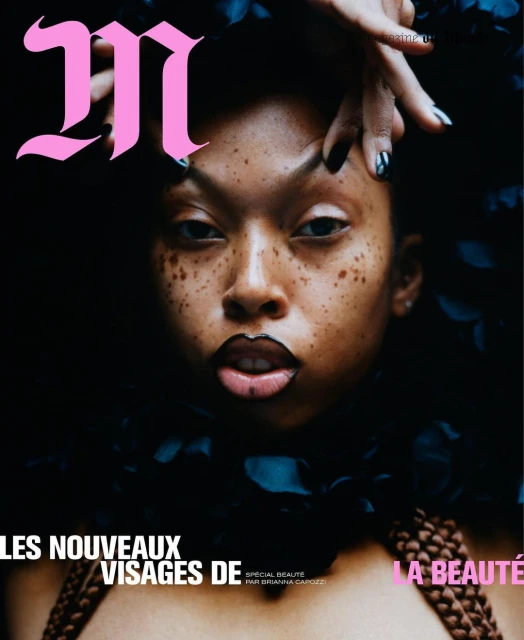 Magazine cover featuring a close-up of a woman with freckles, dark hair, and painted lips, adorned with a pink 'M' logo.