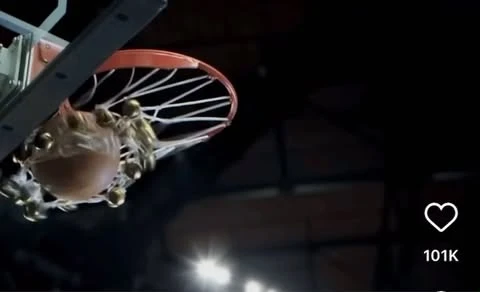 Basketball swishing through the net inside a gymnasium with a dark, neutral color palette in a low-angle shot.