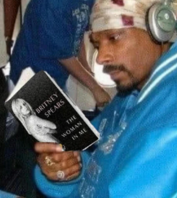 Snoop Dogg is seen indoors, wearing headphones and reading a book titled 'Britney Spears: The Woman in Me'.