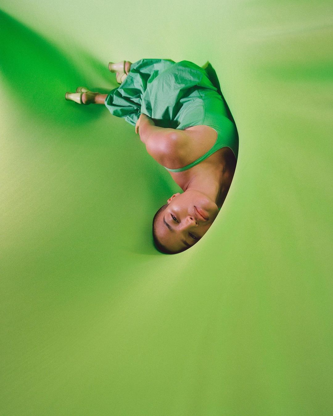 Woman in green dress lies on a green surface. Studio shot with interesting angle and lighting, fashion editorial for creative.