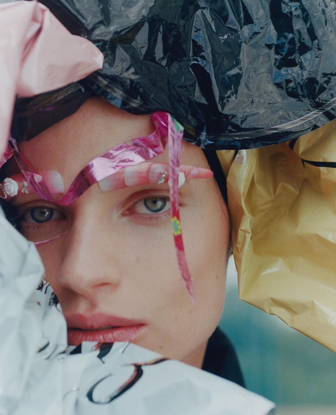 Close-up portrait of a woman surrounded by crinkled plastic packaging and creative makeup by Brianna Capozzi
