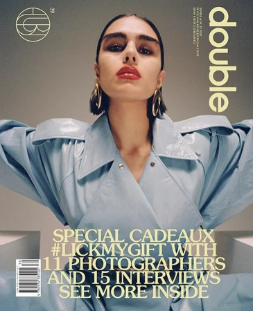 Fashion magazine cover featuring a model in a glossy blue jacket, wearing large hoop earrings and bold red lipstick, against a neutral backdrop.