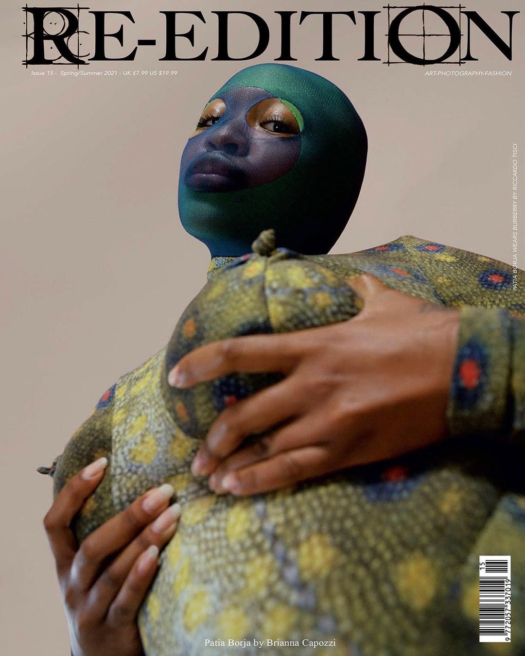 Magazine cover featuring a person in a green patterned outfit and mask, holding a patterned object against a light-tan background.