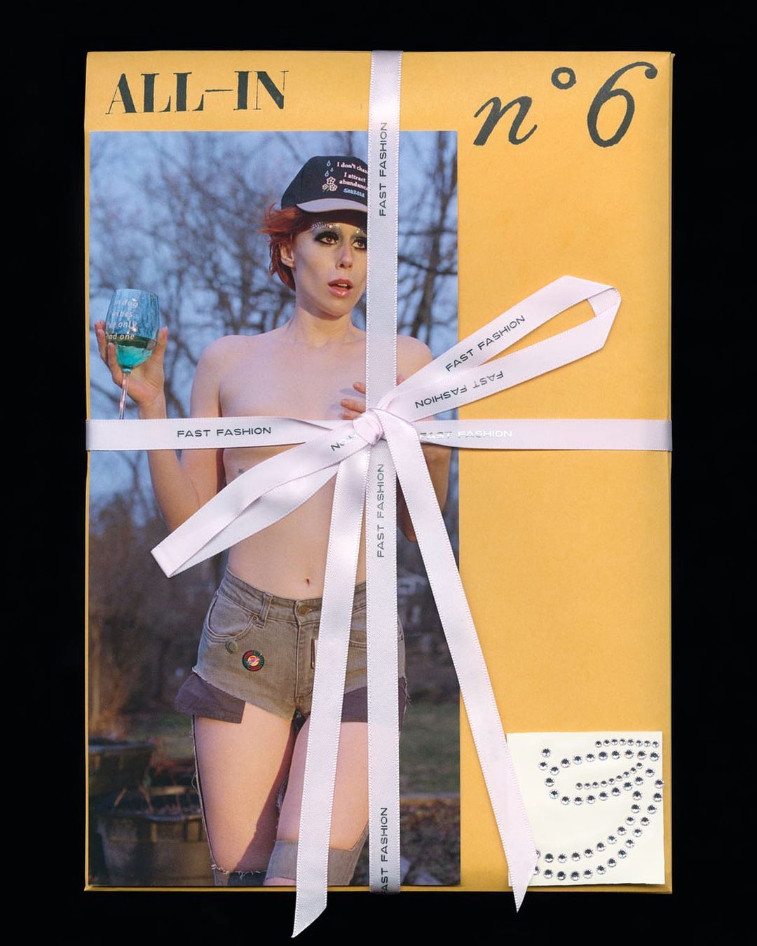 Person on package cover with cocktail glass, wearing hat and denim shorts, tied with ribbon and with number six visible.