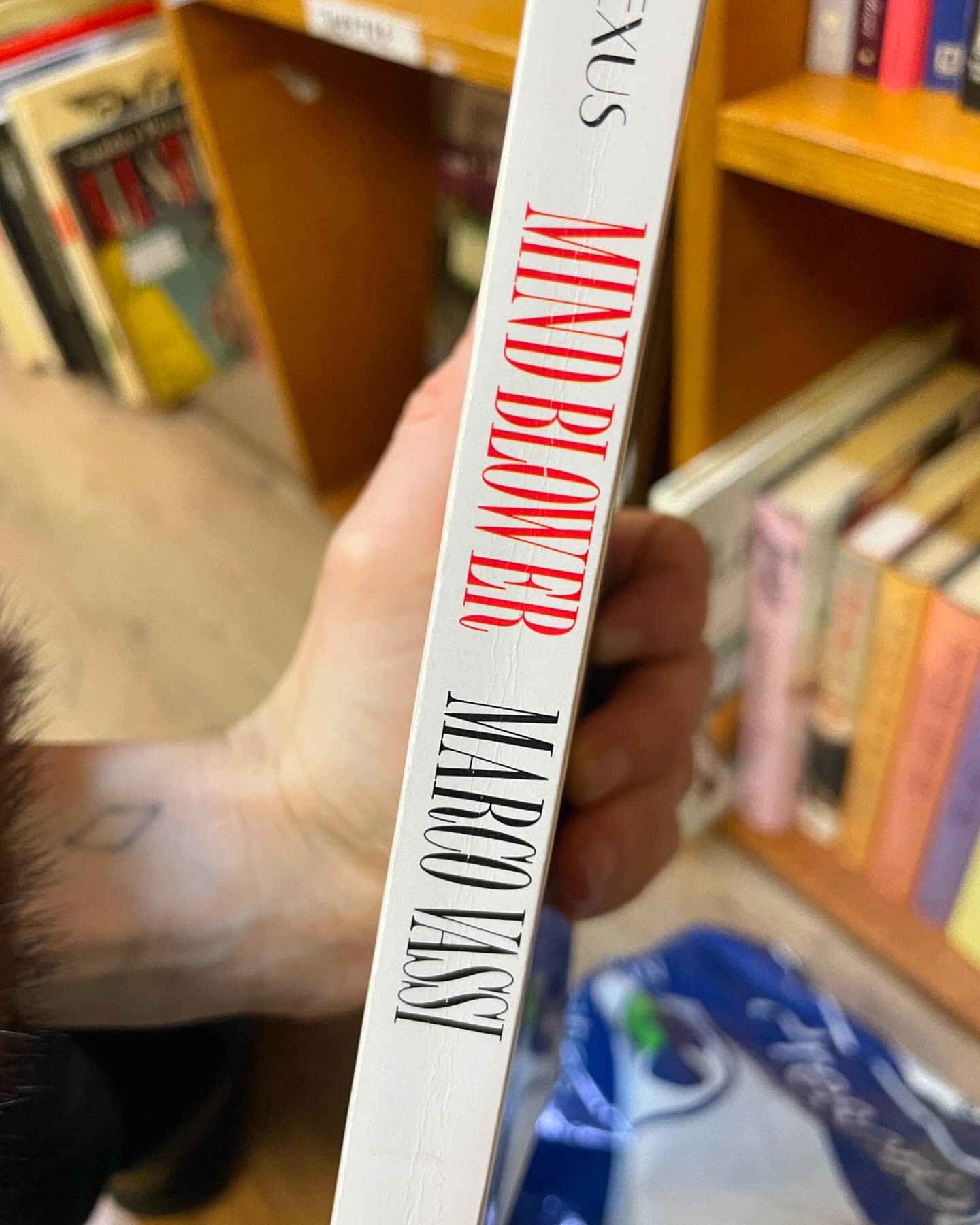 Close-up of a book spine with the title 'Mind Blower' by Marco Vassi in red and black lettering. Bookshelf in the background.
