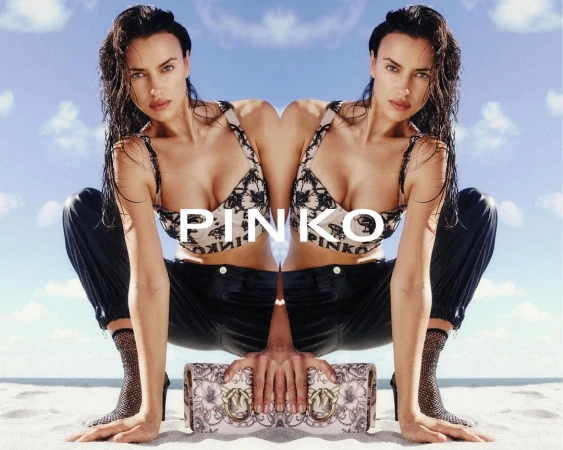Mirrored image of a woman in a bralette and pants, holding a purse, on a sandy beach against a bright sky with few clouds.