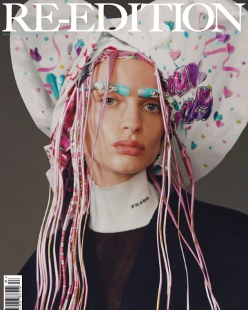 Fashion magazine cover featuring a model wearing a white headscarf, strands of pink hair extensions, Prada top, and light turquoise makeup.