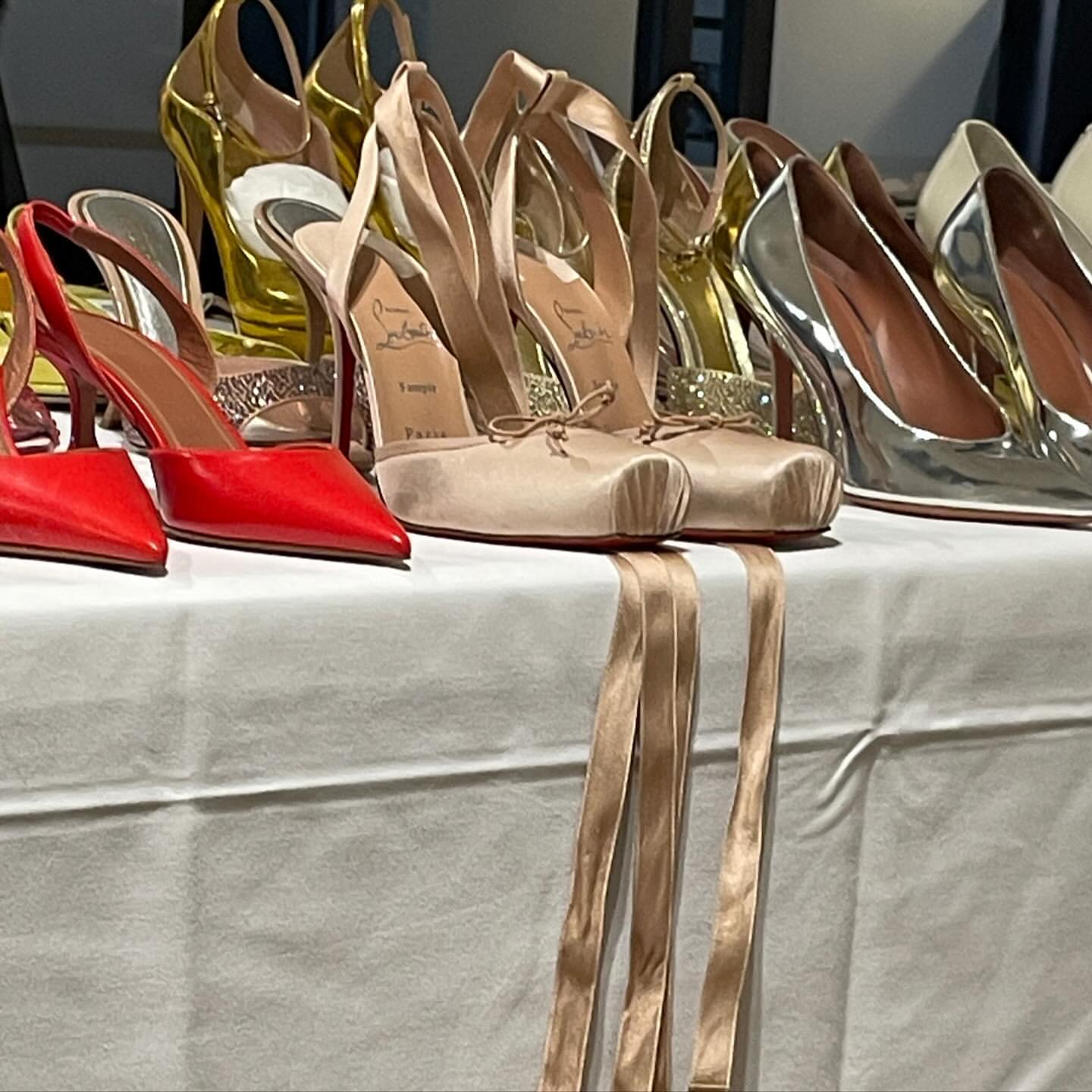 Display of designer high heels in red, silver, gold, and neutral tones with ribbon on a white table for luxury fashion advertising.