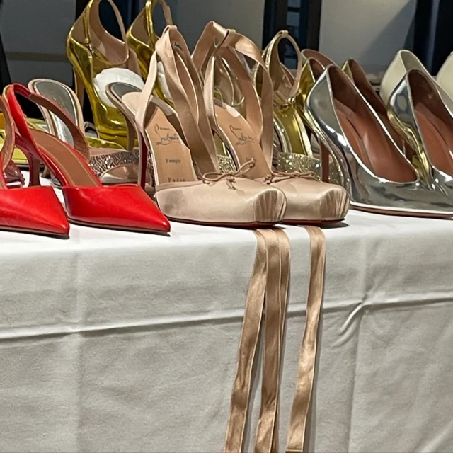 Display of designer high heels in red, silver, gold, and neutral tones with ribbon on a white table for luxury fashion advertising.