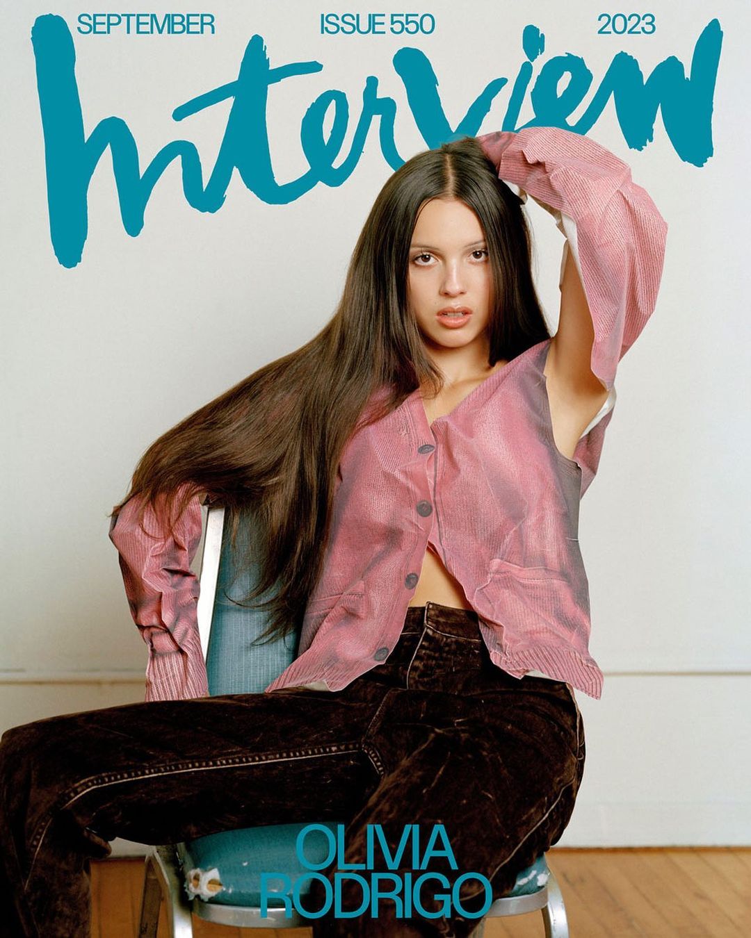 Olivia Rodrigo poses on a chair for an Interview magazine cover with teal masthead, wearing a pink top and brown pants.