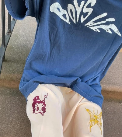 Woman wearing a t-shirt and pants with cartoon designs sitting on steps outside, showcasing casual fashion and streetwear style.