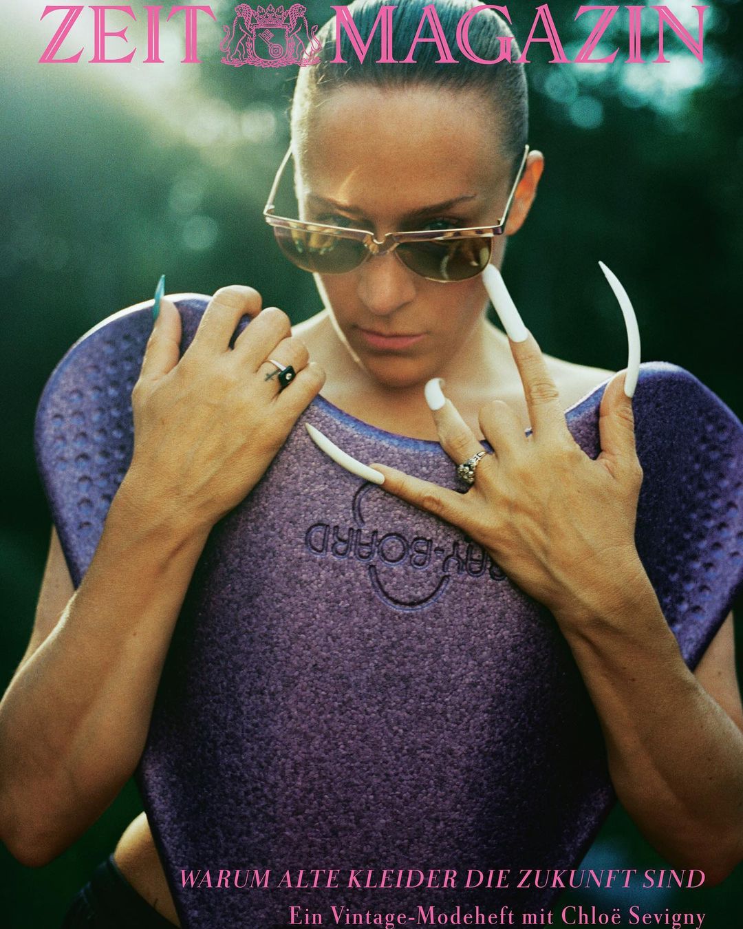 Fashion magazine cover featuring a woman wearing sunglasses and holding a purple bodyboard with extremely long white fingernails.
