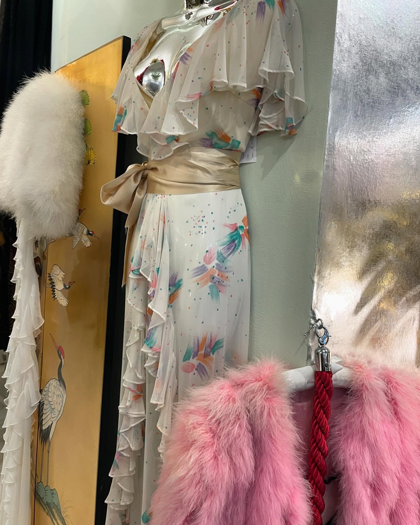 Elegant white floral dress with ruffles and a satin belt on display alongside vintage accessories in a shop, capturing classic style.
