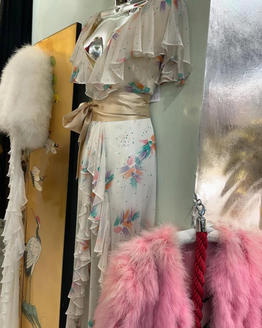 Elegant white floral dress with ruffles and a satin belt on display alongside vintage accessories in a shop, capturing classic style.