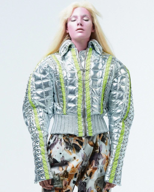 A person with light pink skin and blonde hair wears a silver quilted jacket with lime green accents and pants printed with bunny rabbits.