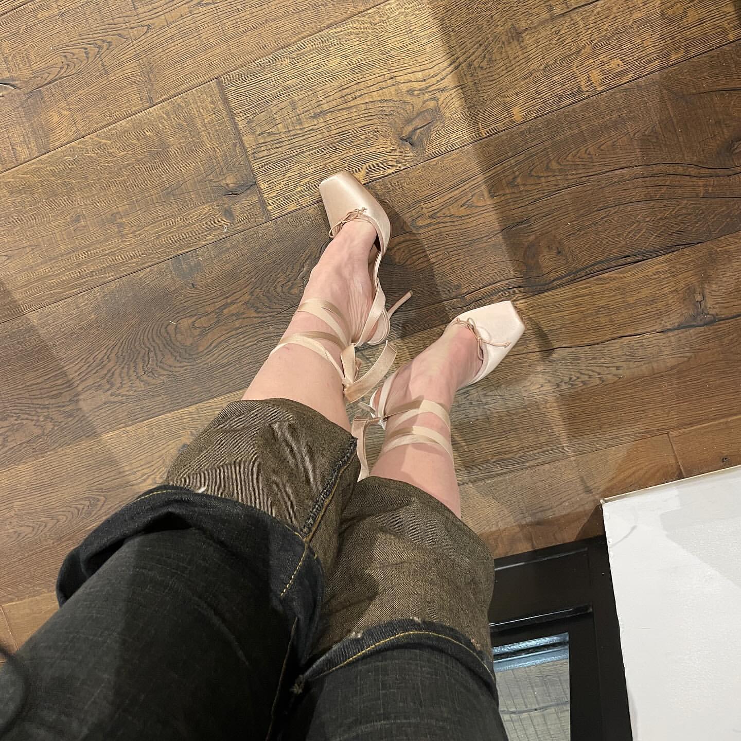A person's legs and feet wearing ballet pointe shoes with ribbon, shot from a high angle on wood flooring, indoor setting.