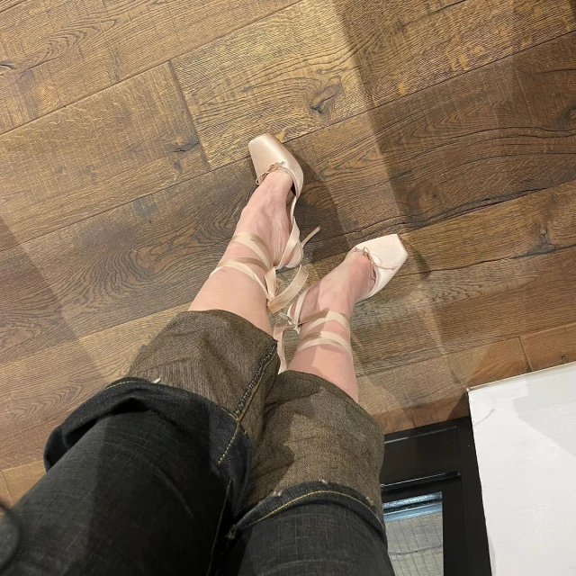 A person's legs and feet wearing ballet pointe shoes with ribbon, shot from a high angle on wood flooring, indoor setting.