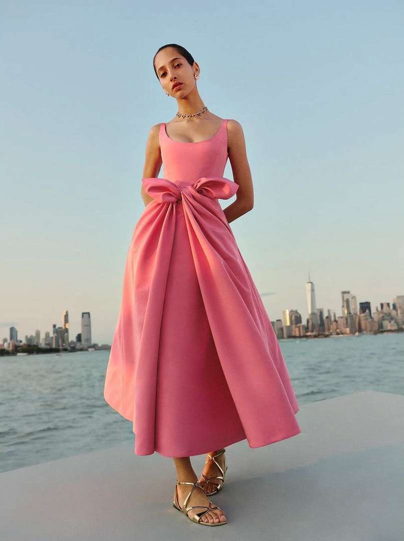 Woman in a pink formal gown posing with a city skyline background in an outdoor fashion shot with a water foreground.