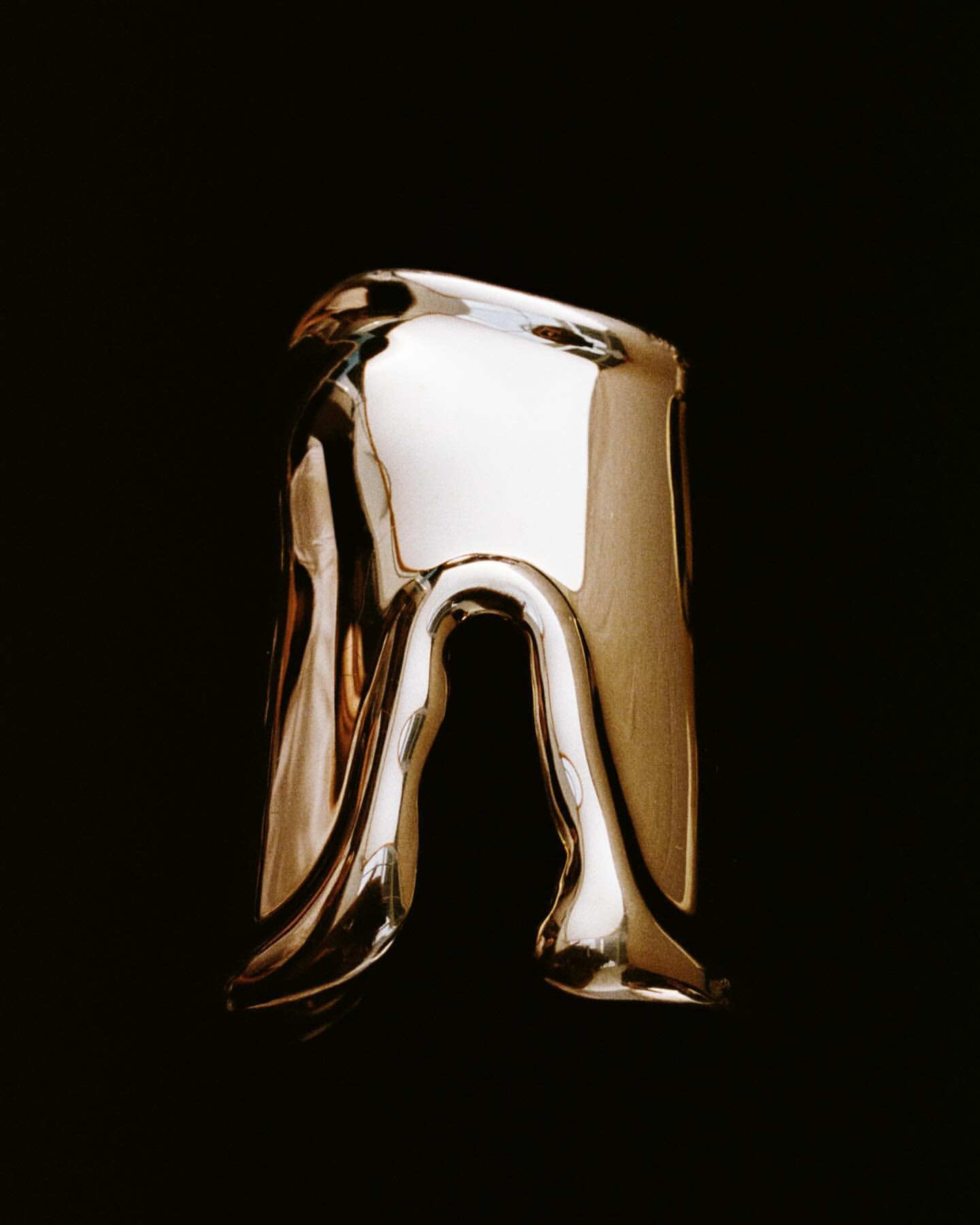 Abstract golden ring with flowing, melting design on a stark black backdrop, high contrast studio lighting, and reflective surface.