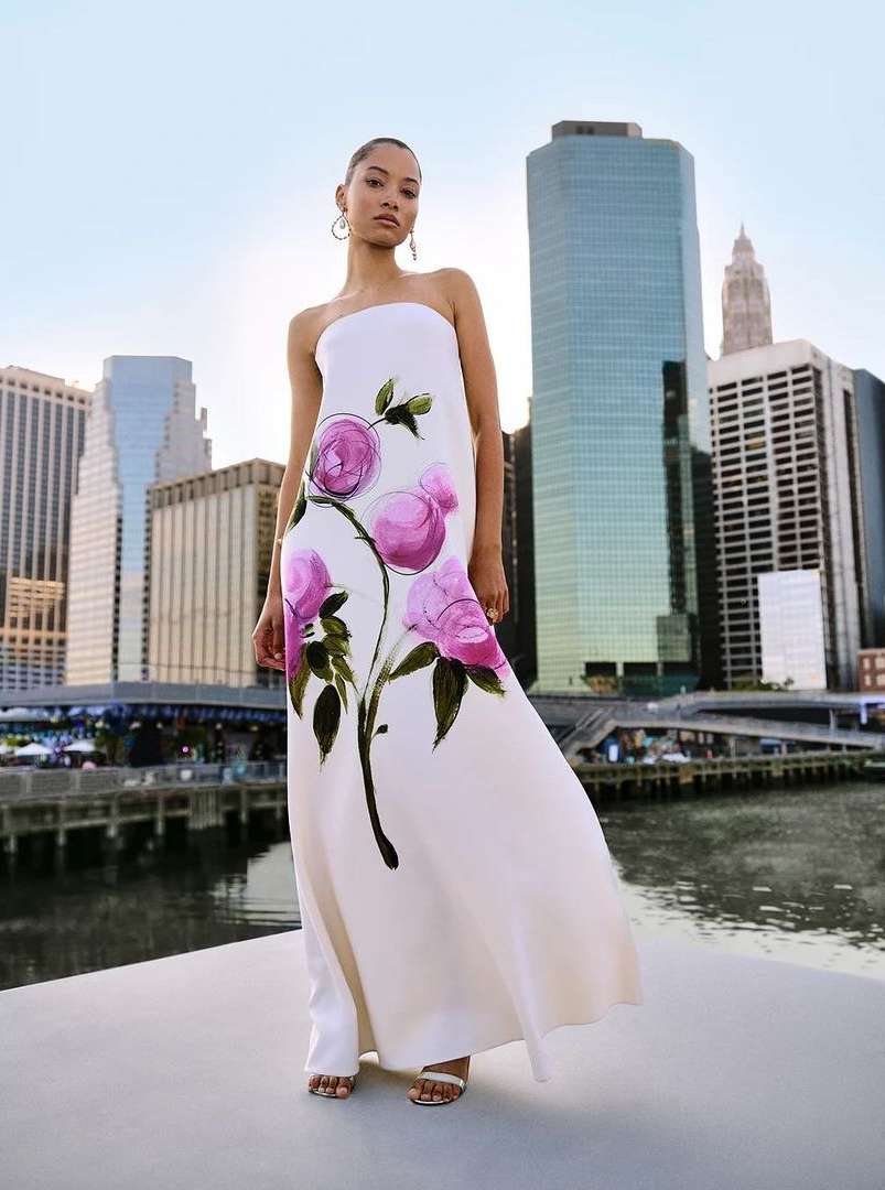 Woman in strapless dress with floral design stands in front of cityscape. Modern fashion shoot with an urban background.