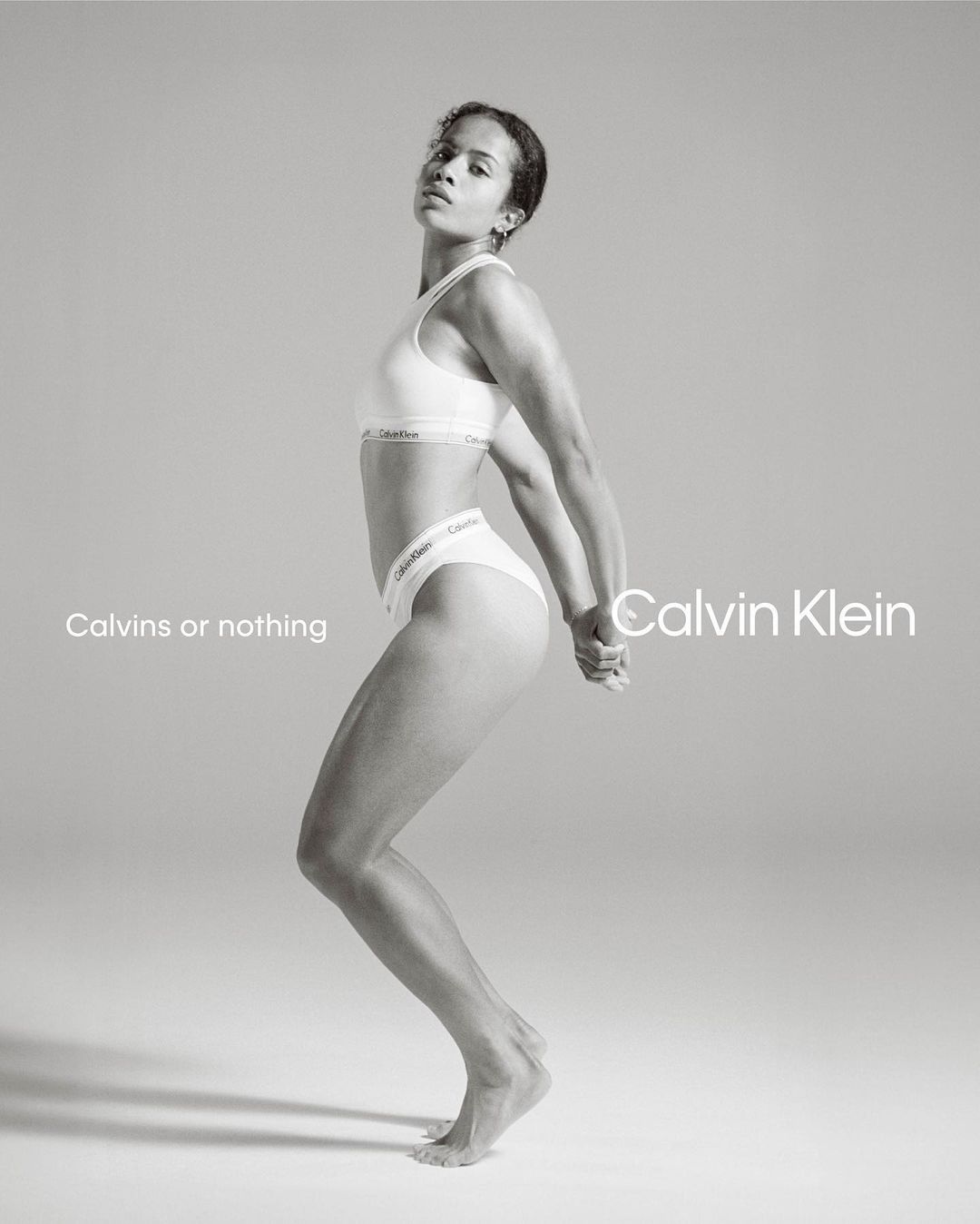 Athletic woman in Calvin Klein underwear strikes a pose in a bright studio. The photo is monochrome, featuring minimalist design elements.