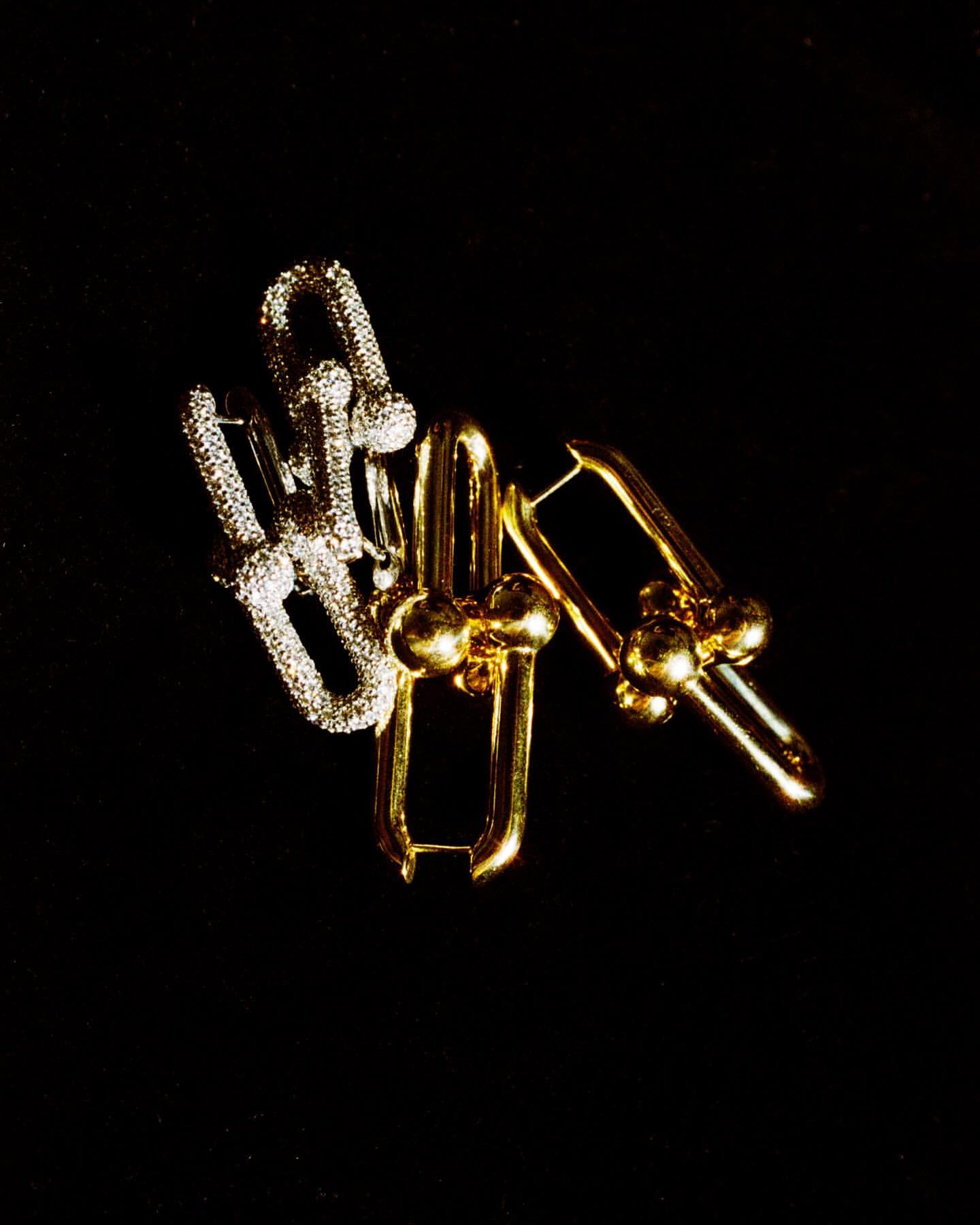 Close-up of two sets of gold and silver colored metal earrings on a black background, lit from above in a jewelry advertisement.