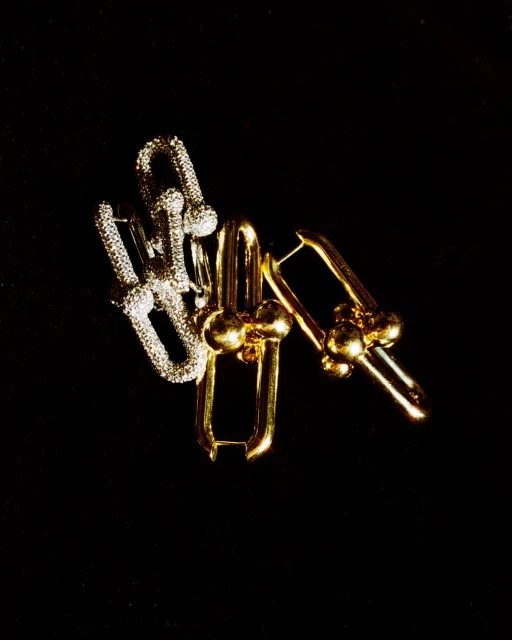 Close-up of two sets of gold and silver colored metal earrings on a black background, lit from above in a jewelry advertisement.