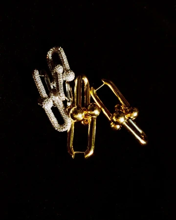 Close-up of two sets of gold and silver colored metal earrings on a black background, lit from above in a jewelry advertisement.
