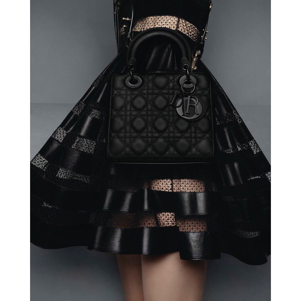 Close-up shot of a black leather Dior handbag, showcasing its quilted texture and craftsmanship, complemented by a black dress.