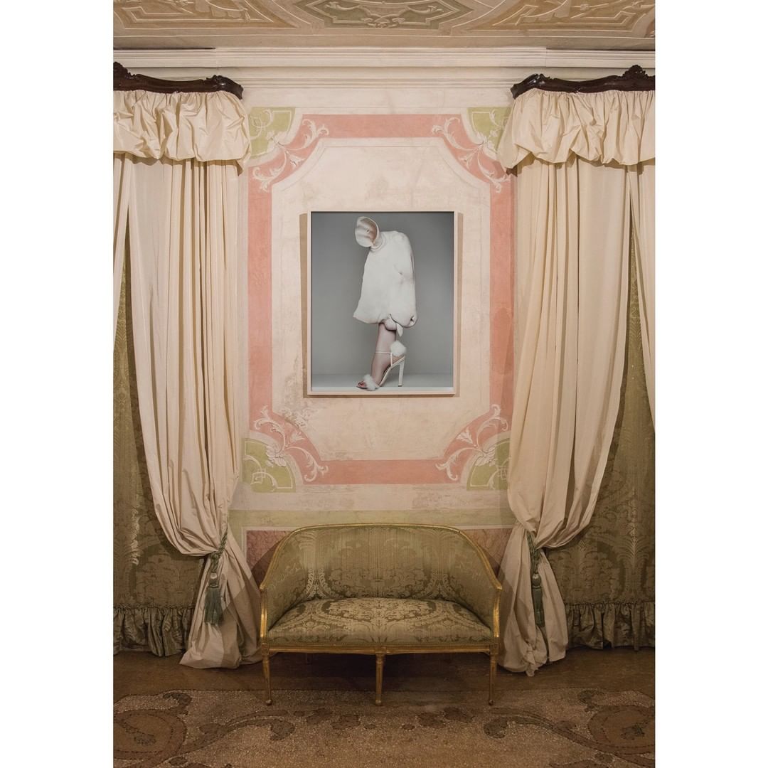Fashion photography of white stiletto heel, dress, and decorative wall inside a room with vintage couch and curtain details. 