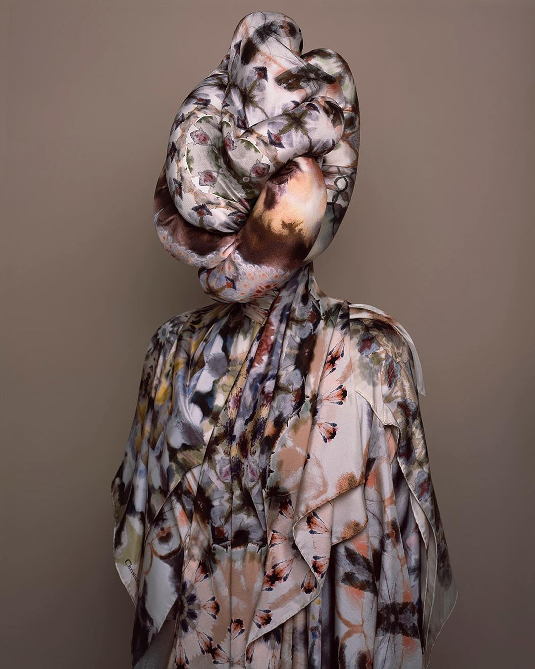 Abstract fashion portrait of a person covered in a floral patterned textile, obscuring the face with a knotted fabric headpiece.