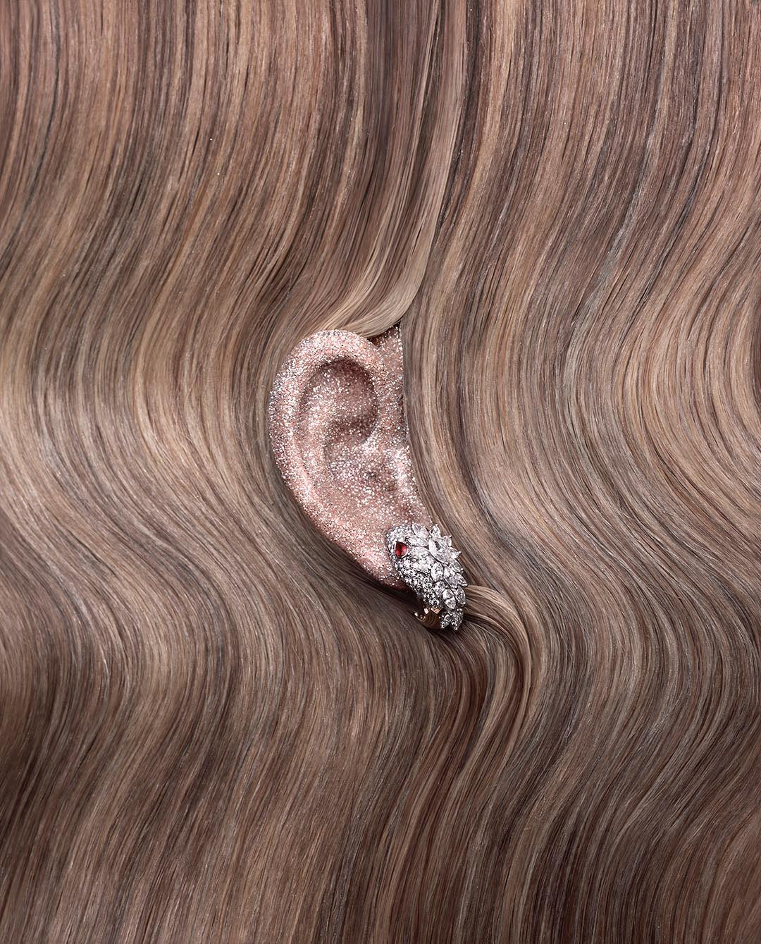 Close-up of an ear with a diamond earring, surrounded by blond hair, showcasing the earring's sparkle and elegance.