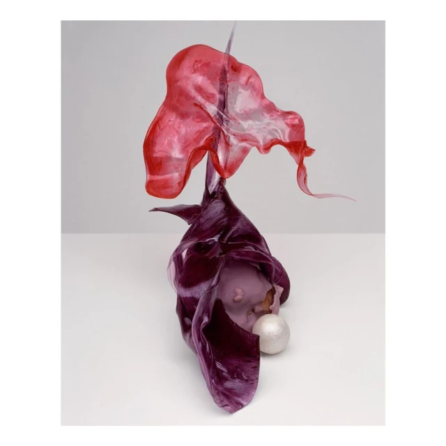 Abstract still life with iridescent red and purple fabric arranged around a white orb on a light gray studio backdrop.