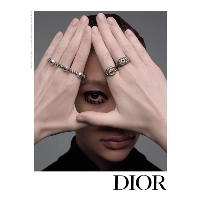 Close-up fashion shot featuring a person with graphic eyeliner, posing with hands framing their face to display rings and a bracelet.