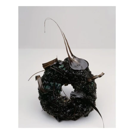 Abstract art piece featuring a dark, textured, donut-shaped object adorned with glossy, dark-colored, organic elements, against a plain background.