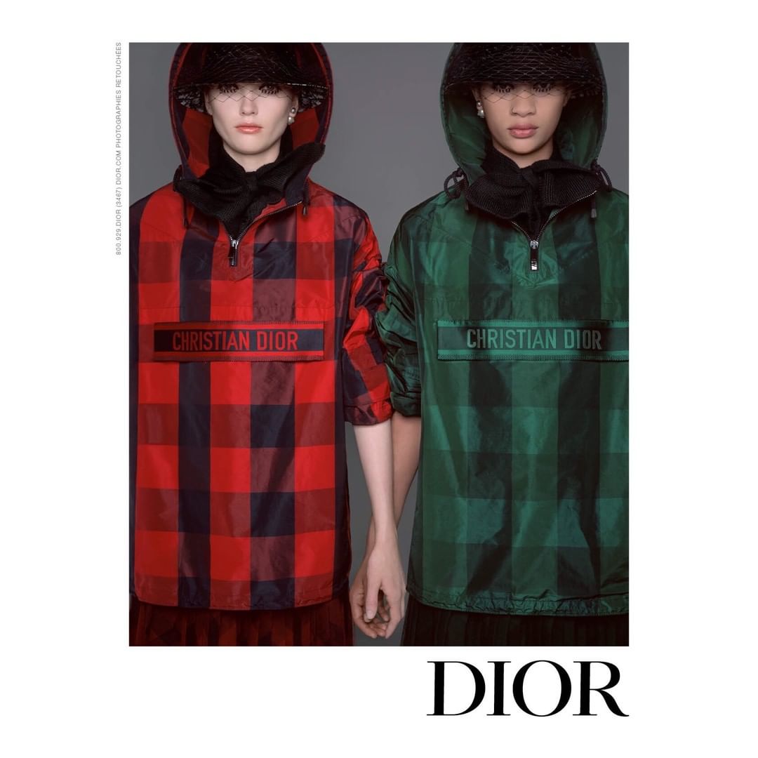Two fashion models in hooded plaid jackets, one red and one green, pose against a gray background, showcasing a modern streetwear style.