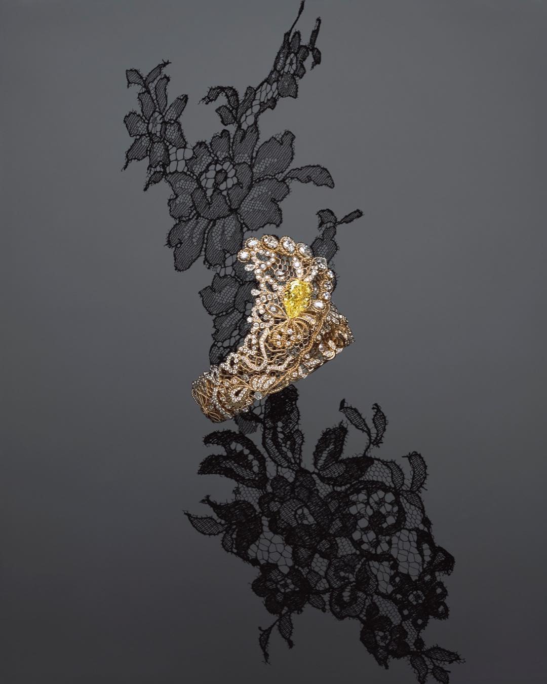 Ornate gold bracelet with yellow gemstone on black lace with reflection, product shot for jewelry and fashion industries.