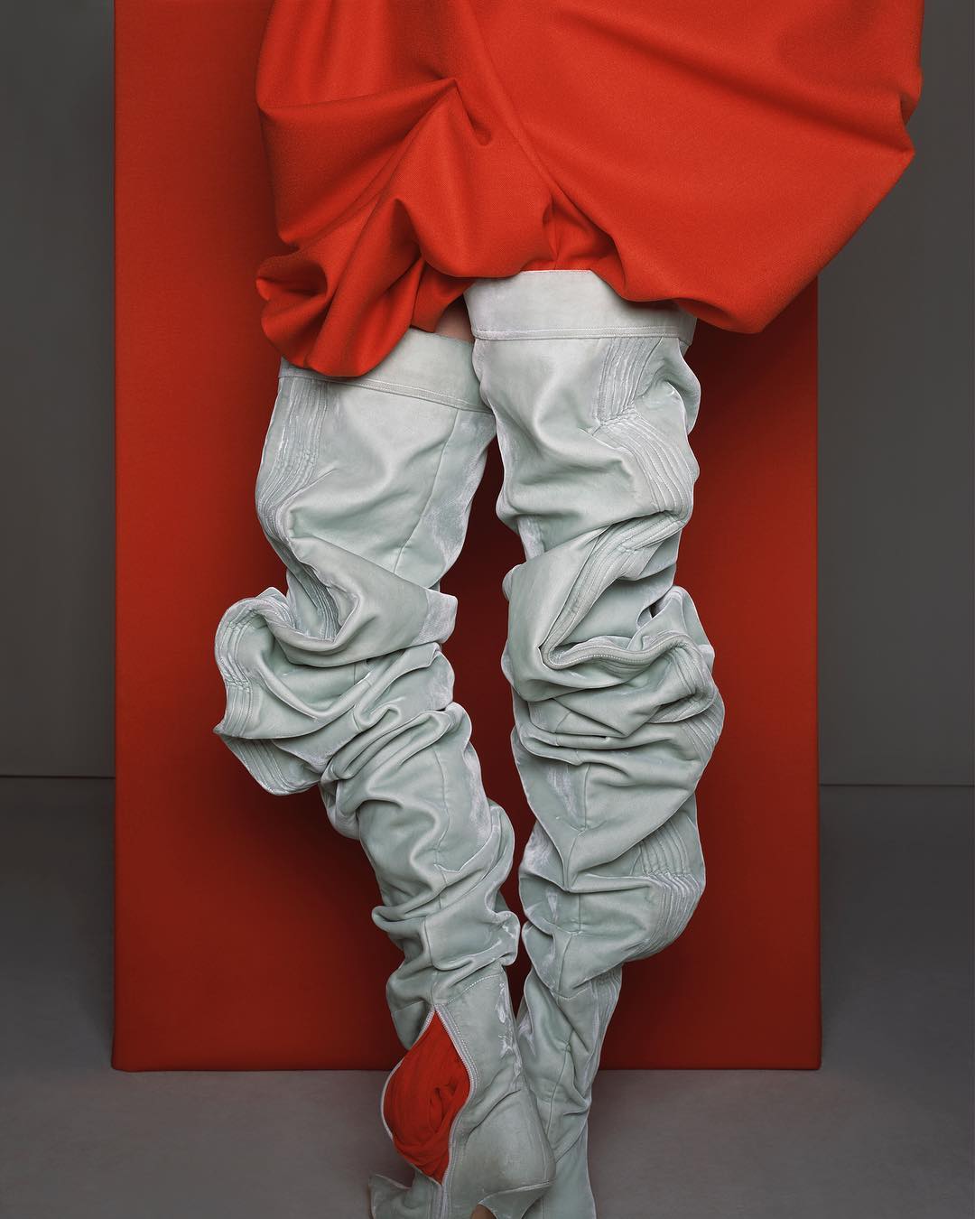 Fashionable textile thigh-high boots on legs, paired with a red garment, against a vibrant red backdrop and grey background.