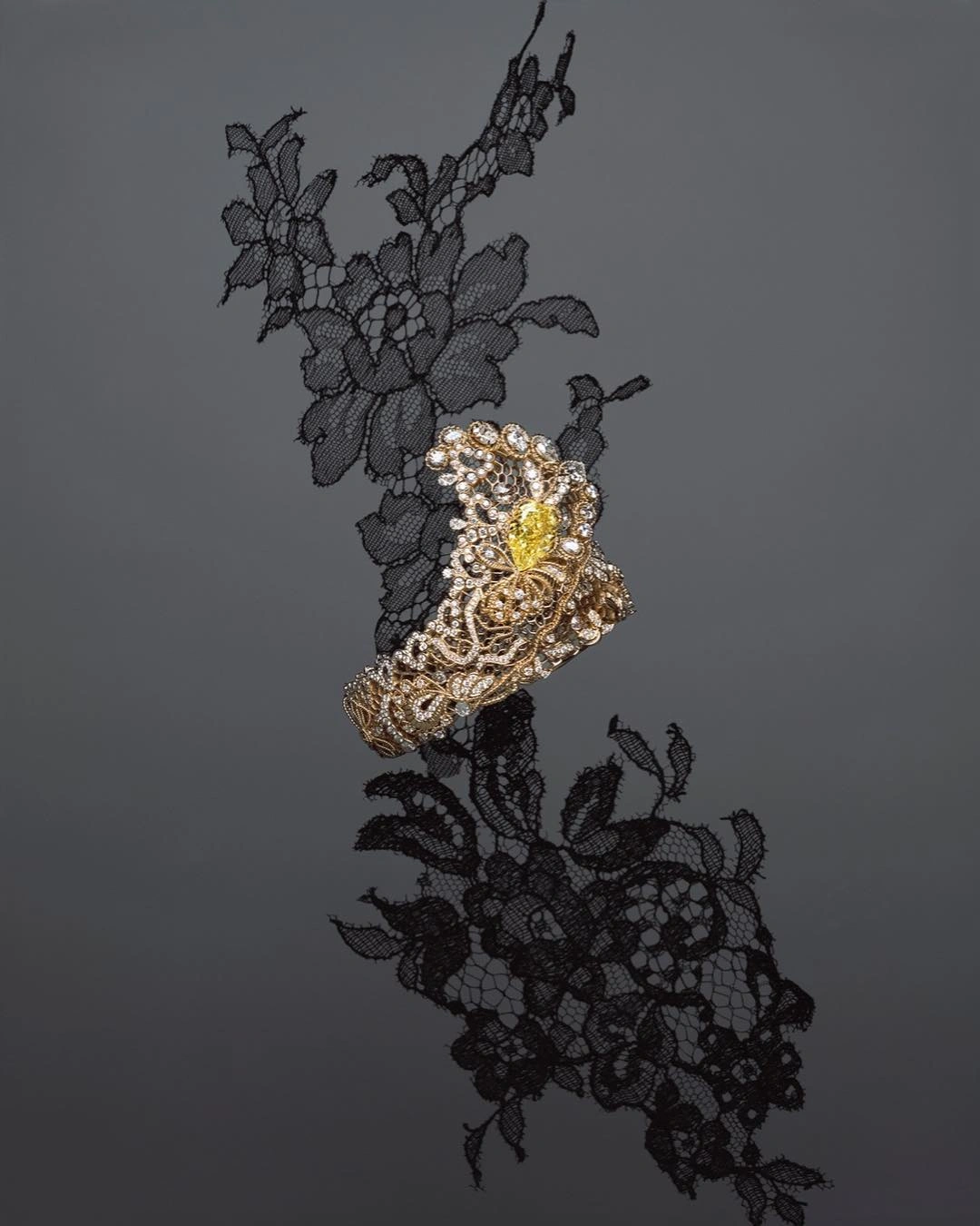 Close-up jewellery photography of a diamond and yellow gemstone cuff bracelet resting on black floral lace.