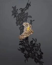 Close-up jewellery photography of a diamond and yellow gemstone cuff bracelet resting on black floral lace.