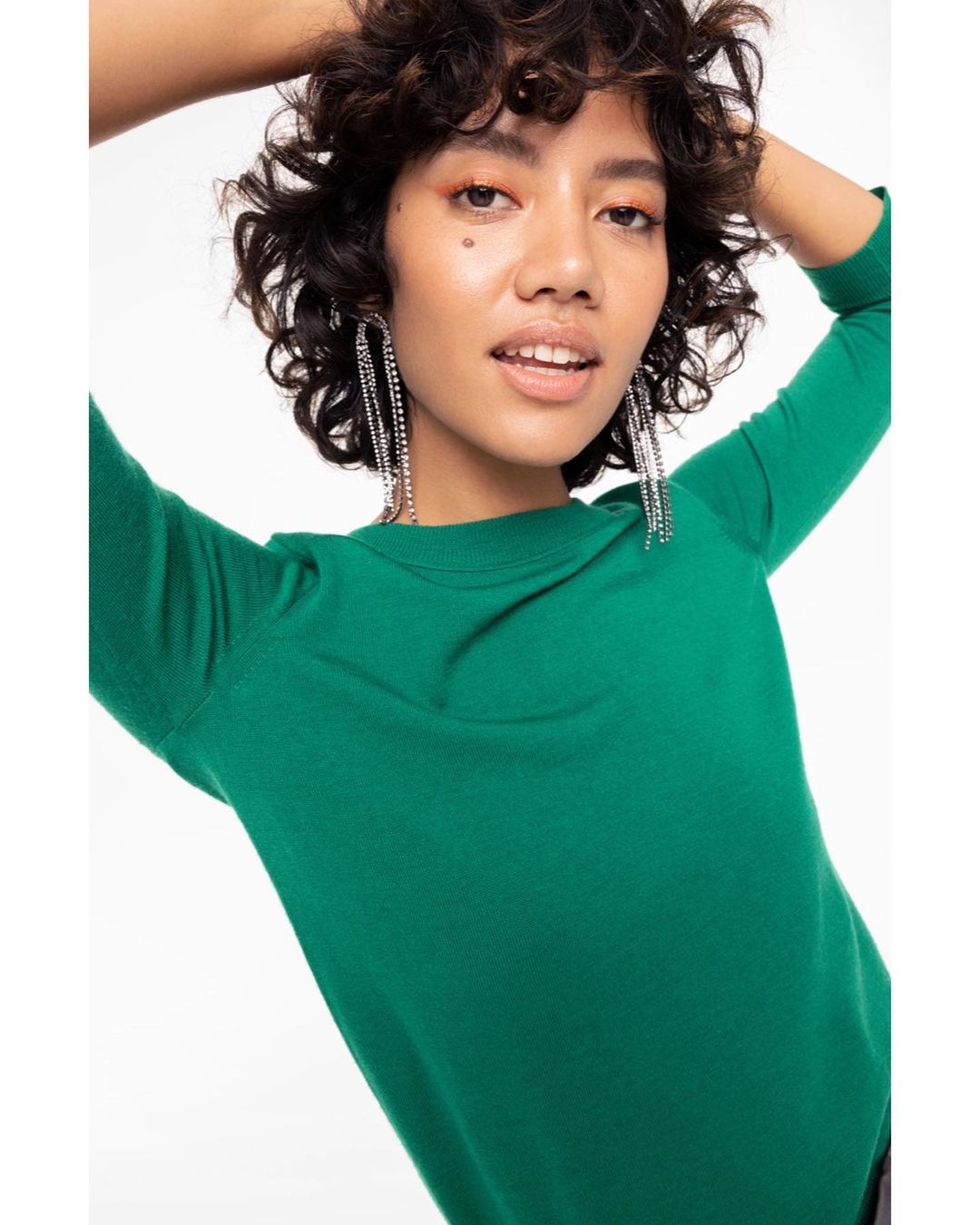 Woman in green sweater posing in a studio with chandelier earrings looking at the camera. Fashion and beauty shot.