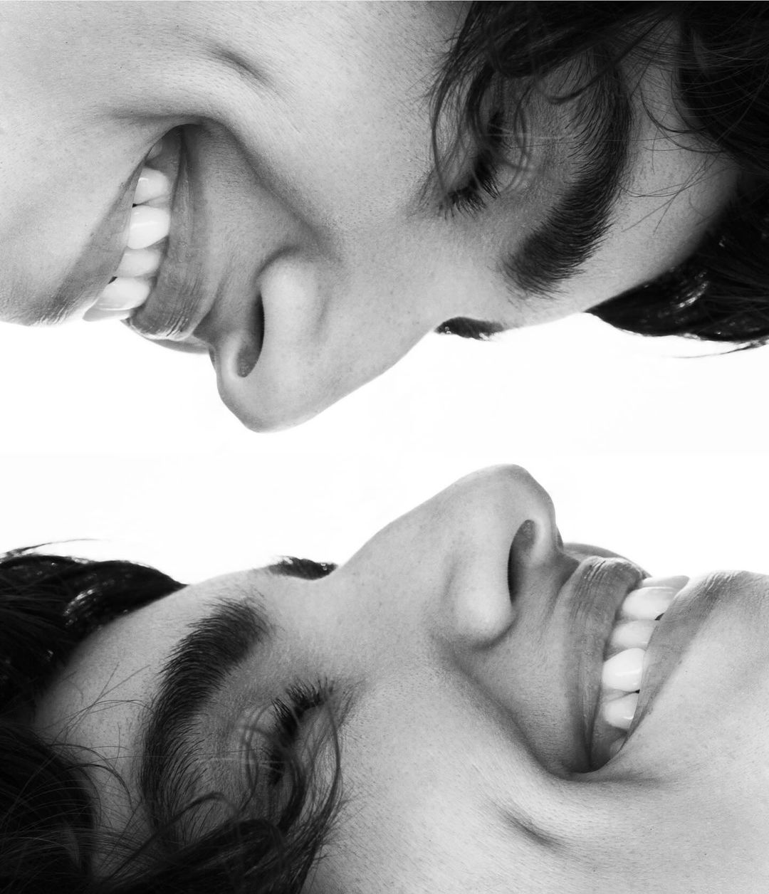 Black and white portrait featuring two smiling faces in mirrored orientation, showcasing joyful expressions and contrasting light and shadow.